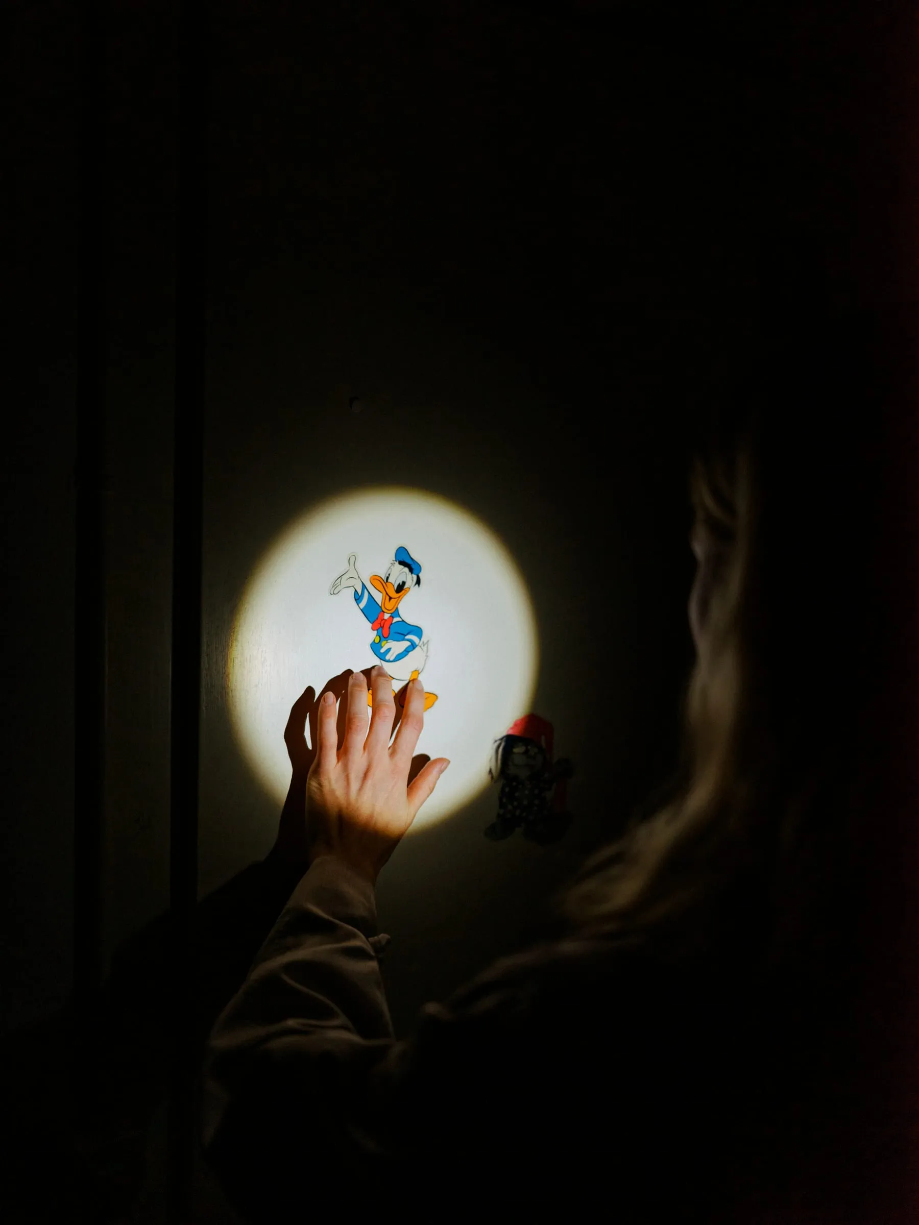 Eine Hand greift im Dunkeln nach einer leuchtenden Scheibe, auf der eine Donald-Duck-Figur abgebildet ist.