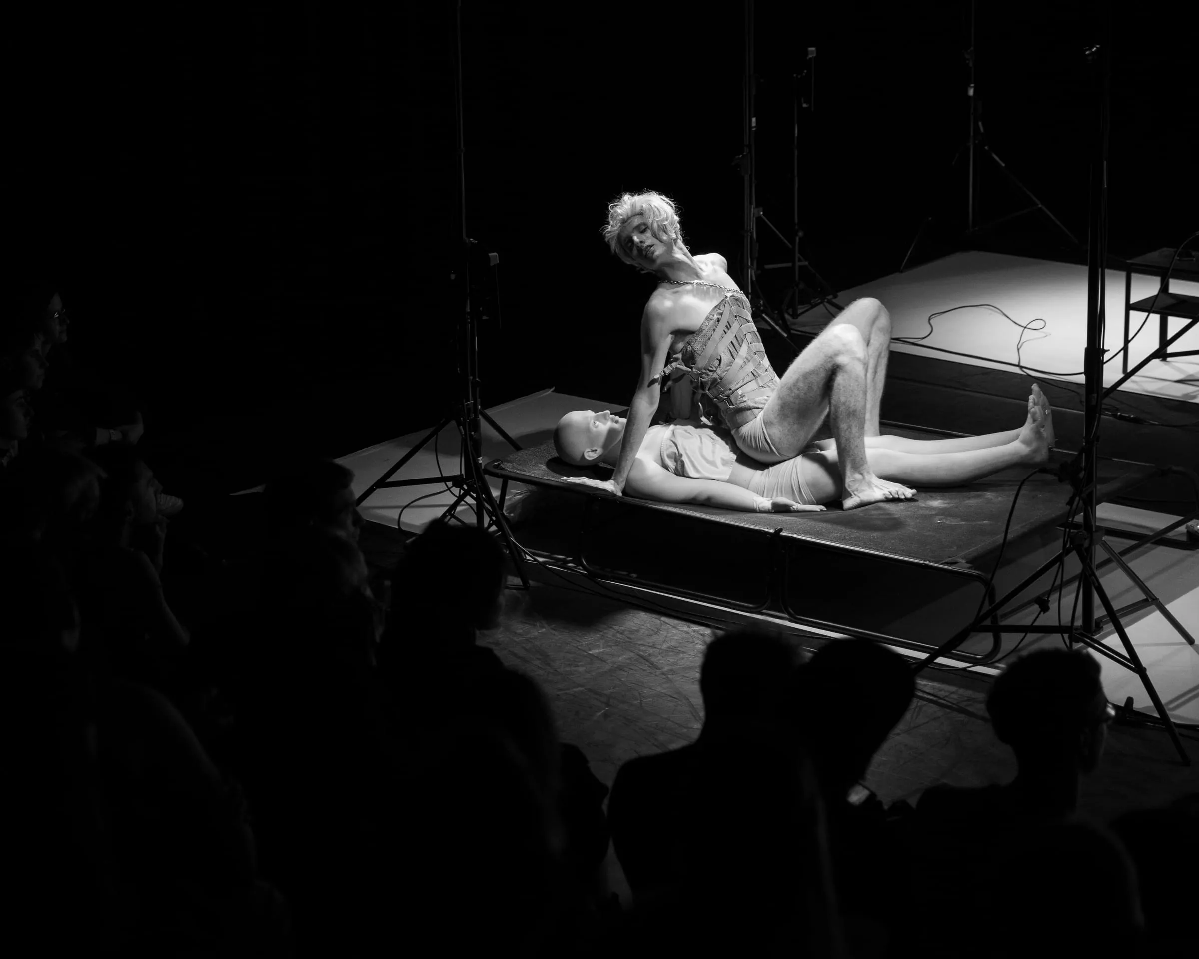 Schwarzweiß: Eine Figur lehnt auf einem Podest, daneben Stative und Kabel.
