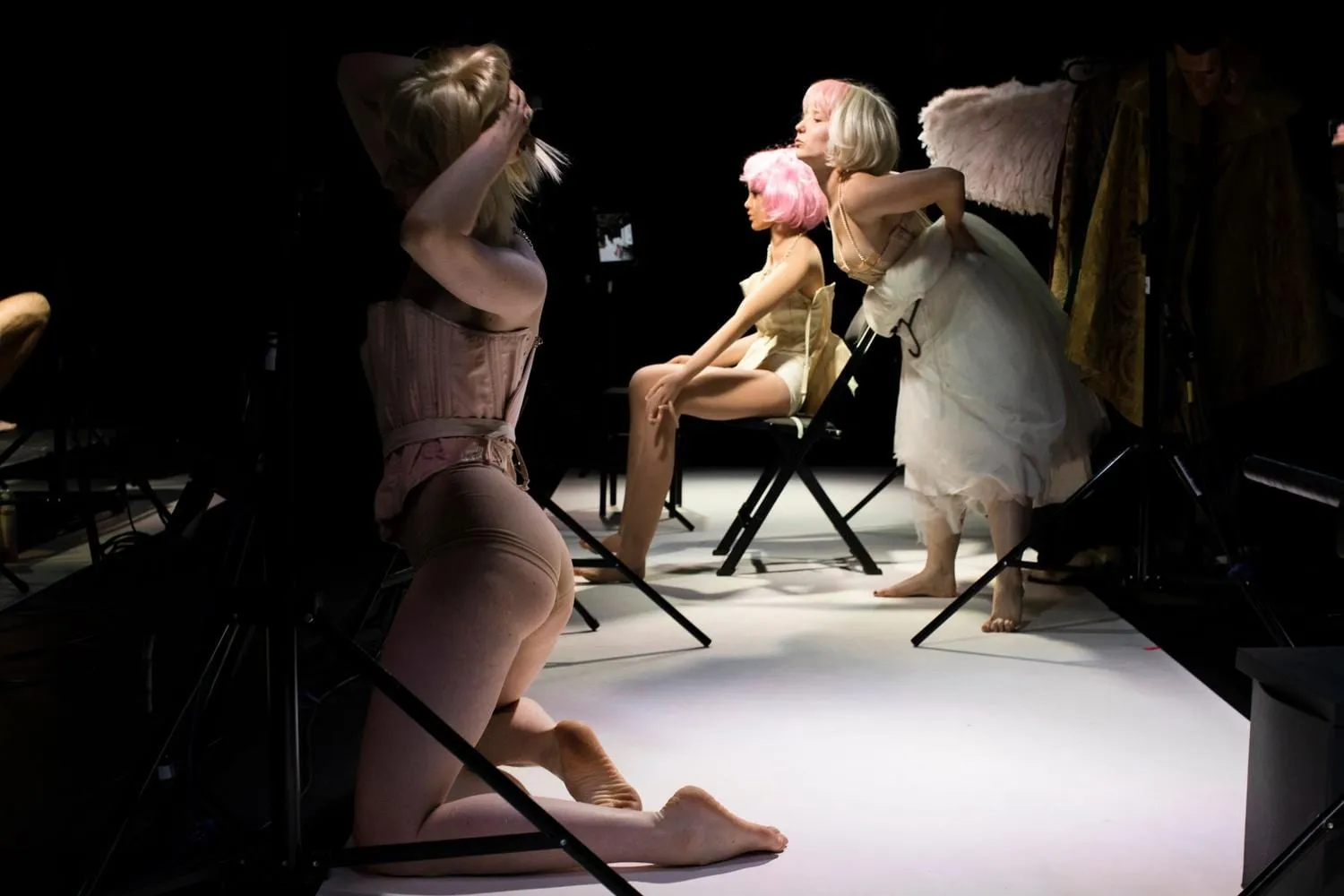 Auf einer weißen Bühnenfläche knien und sitzen Performerinnen zwischen Puppen und Perücken.