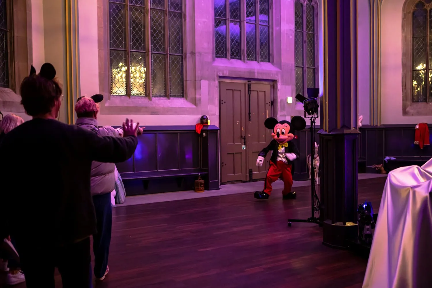 Im Innenraum hebt eine Person die Arme, dahinter sitzt eine rot gekleidete Micky-Maus-Figur an einem Tisch.