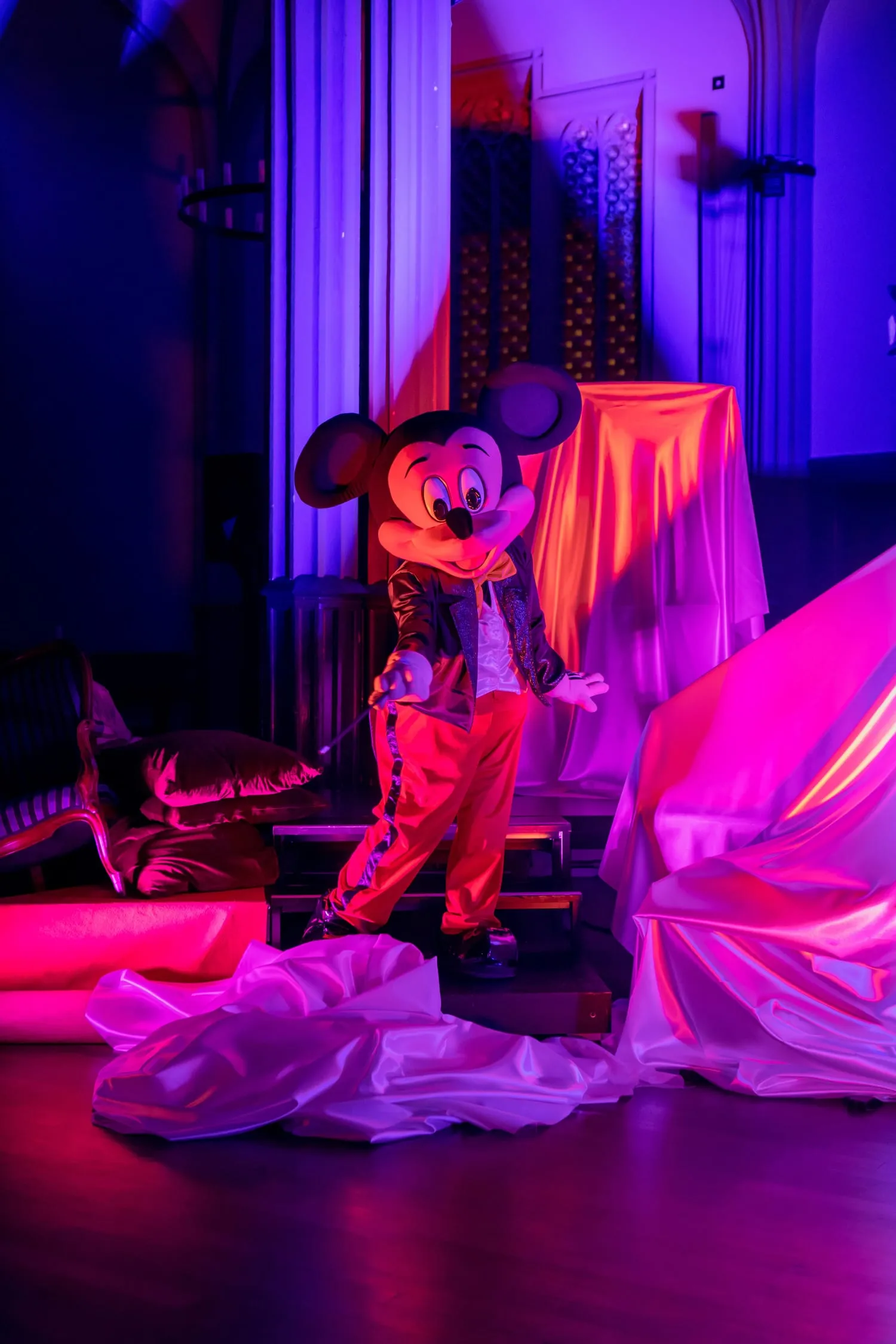 Micky sitzt auf einem Podest zwischen weißen Stoffbahnen, in blaues und rotes Licht getaucht.