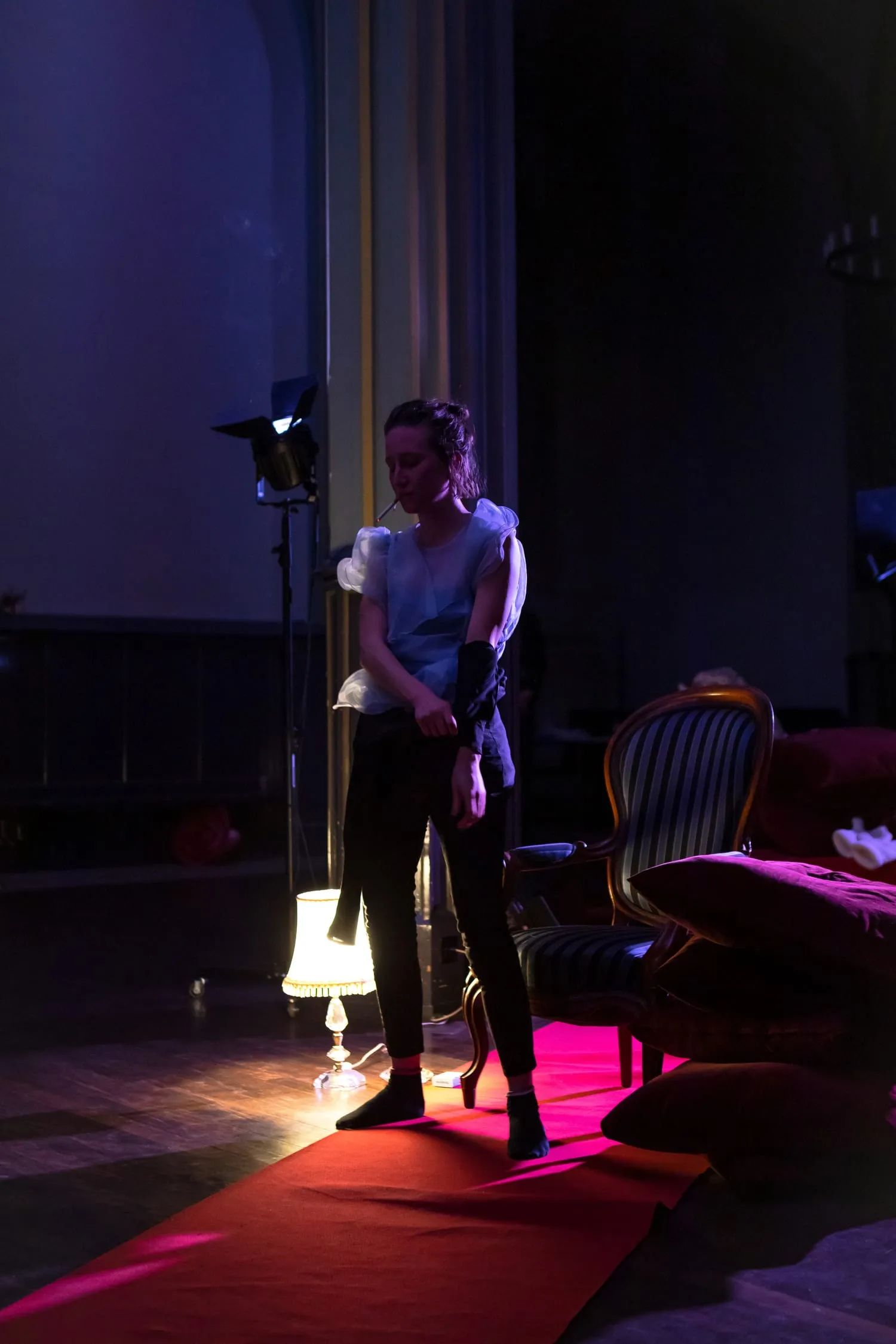 Eine Performerin steht neben einer Stehlampe auf einem roten Teppich.