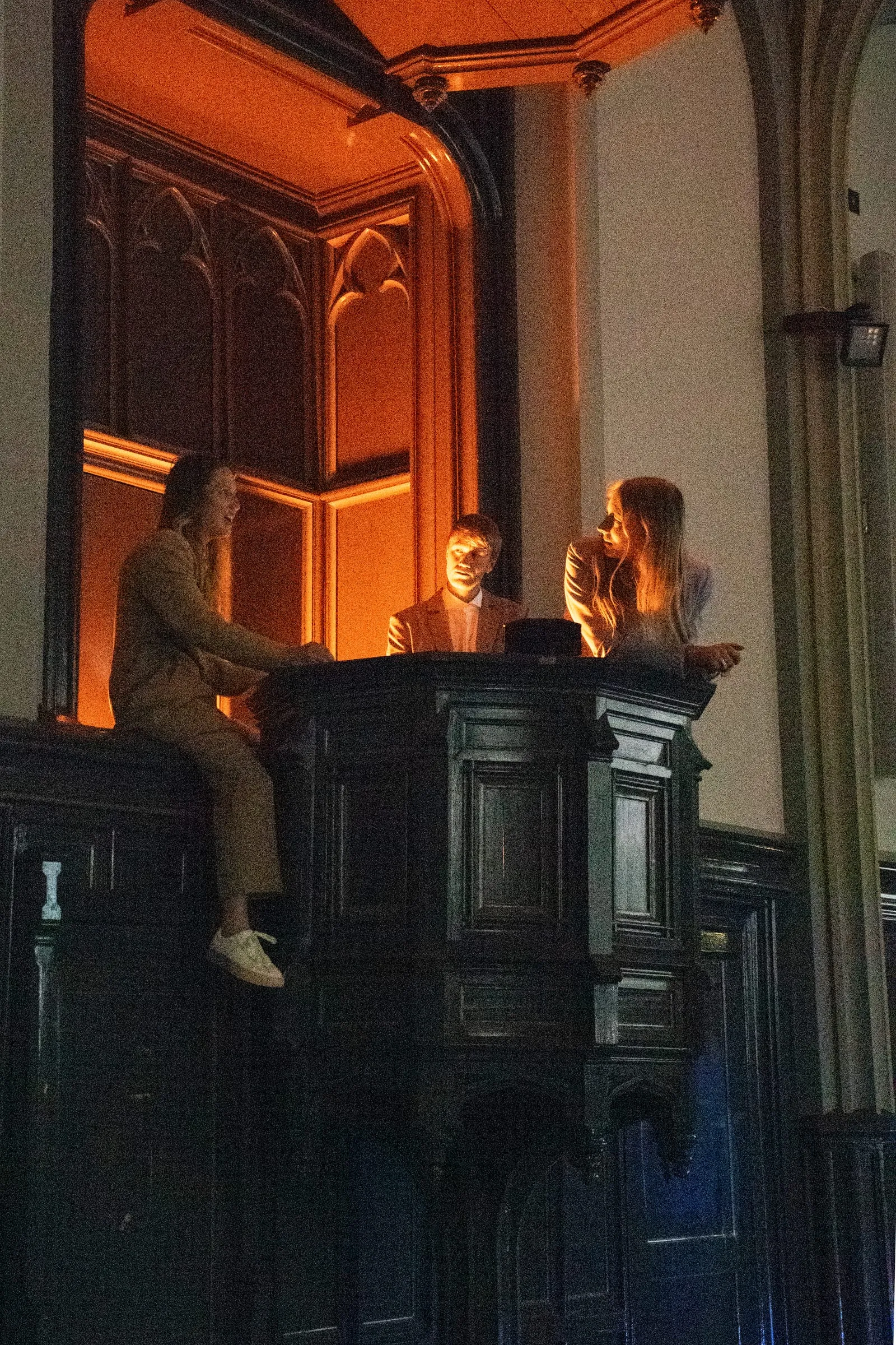 Zwei Figuren auf einer Empore im orange beleuchteten Kirchenraum.